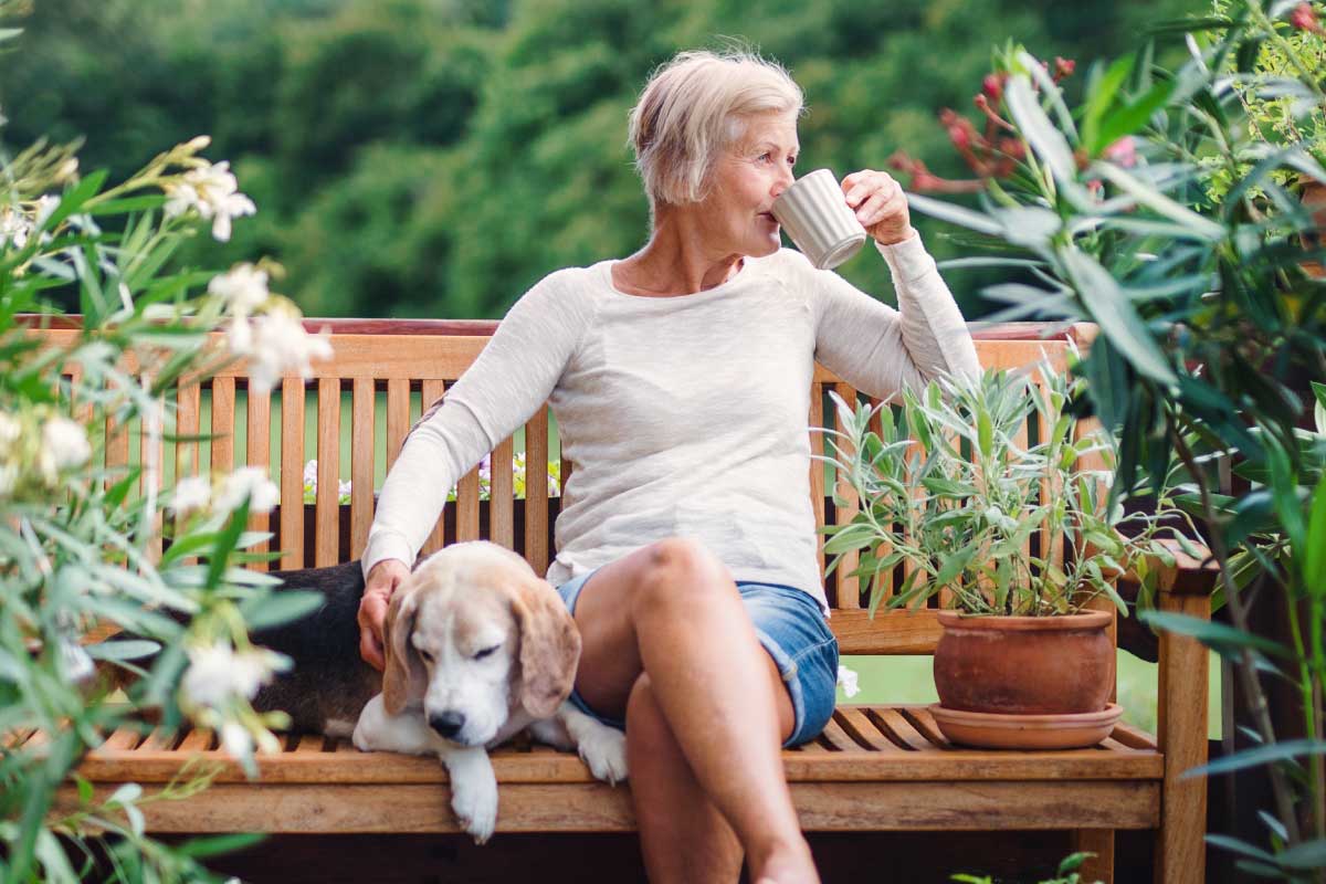 Older lady drinking coffee on a bench with a beagle dog