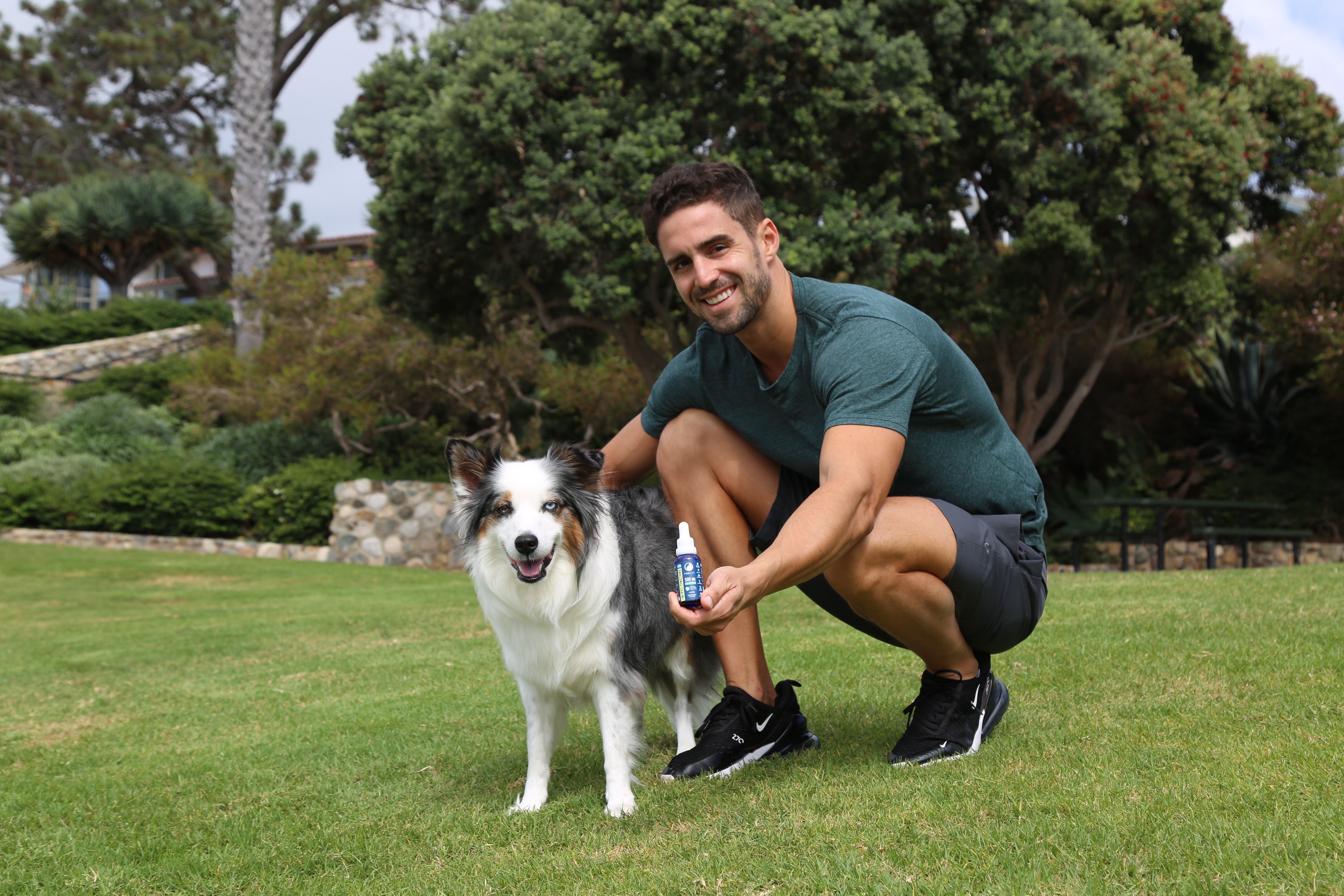 Man, dog on grass holding cbd pet tincture bottle