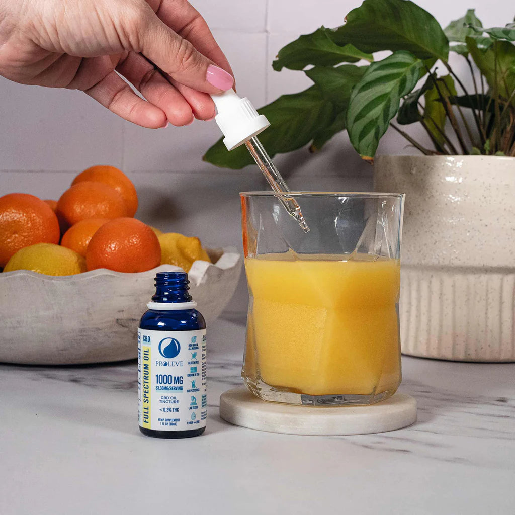 Hand using a dropper to add 1000mg CBD Tincture into a glass of orange juice