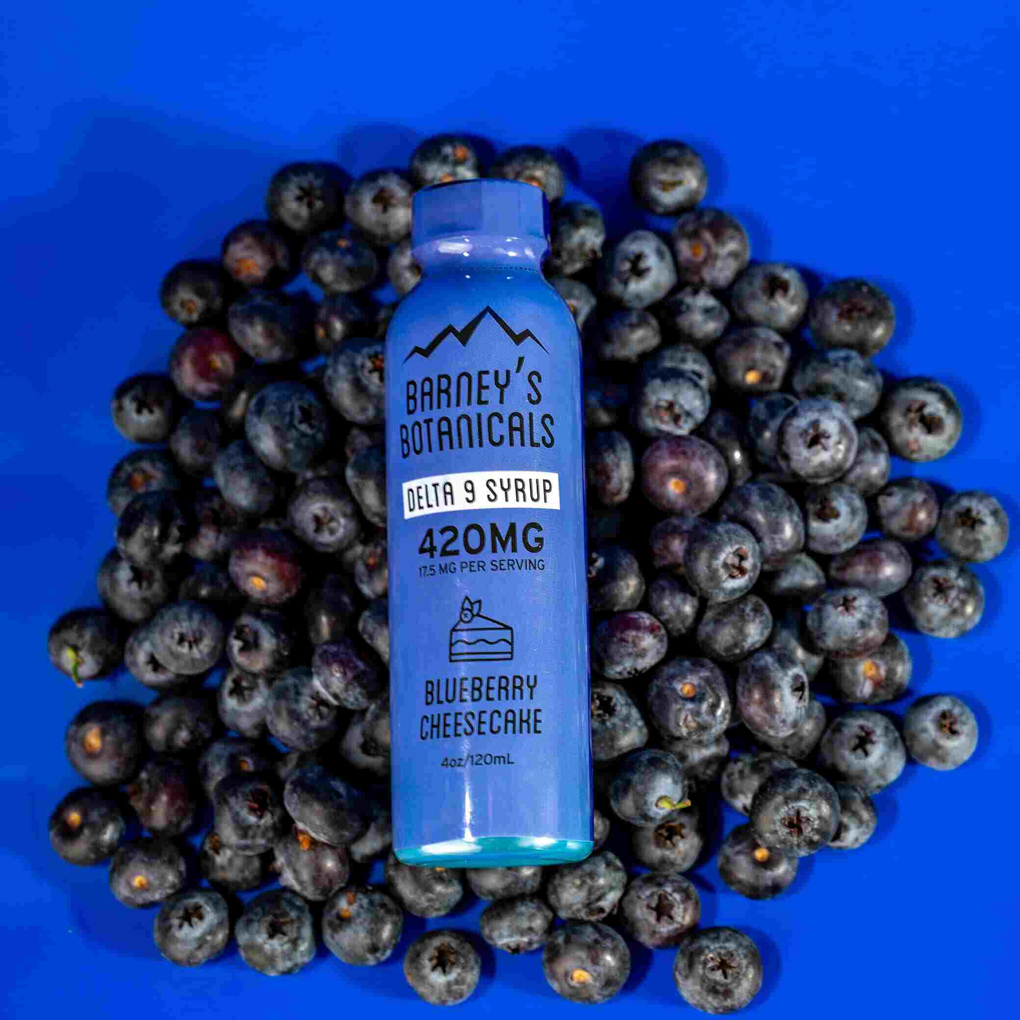 Blue bottle of Barney's Botanicals Delta 9 Syrup surrounded by blueberries on a blue background
